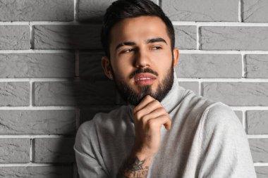 Gri tuğla duvarın yanında dalgın sakallı adam