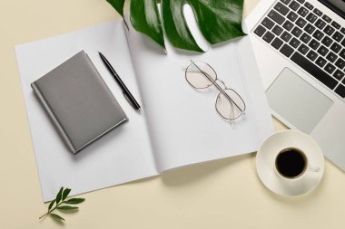 Modern laptop, notebooks, cup of coffee and tropical leaf on yellow background