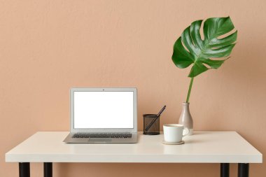 Laptoplu modern işyeri ve bej duvarlı tropikal yapraklı vazo