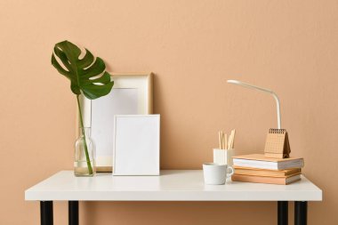 Boş fotoğraf çerçeveleri, kırtasiyesi ve bej duvarın yanında tropikal yaprağı olan vazosu olan şık bir iş yeri.