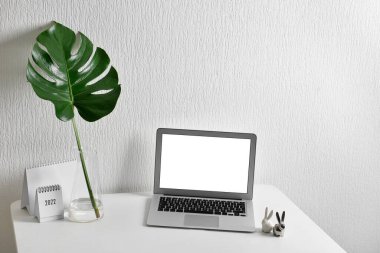 Dizüstü bilgisayarlı iş yeri, vazoda palmiye yaprağı ve ışık duvarına yakın takvim