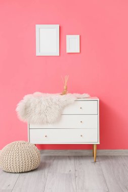Sazlık ayırıcılı çekmeceler ve pembe duvarın yanında puf.