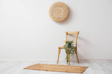 Basket with books and houseplant on chair near light wall