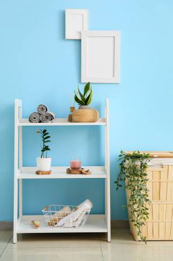 Banyo malzemeleri ve çamaşır sepetinin bulunduğu raf mavi duvarın yanında.