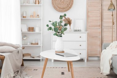 Oturma odasındaki masada okaliptüs dalları ve dizüstü bilgisayarlı vazo.