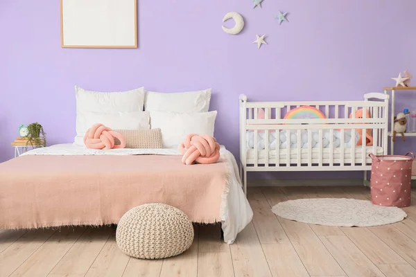 快適なベッドと紫色の壁の近くにベビーベッド付きの寝室のインテリア — ストック写真