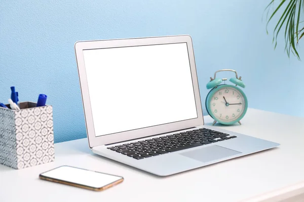 Modern dizüstü bilgisayar, cep telefonu ve alarm saati renk duvarının yanındaki masada.