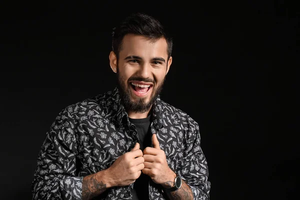 Duygusal sakallı adam koyu arkaplanda gömlek ayarlıyor.