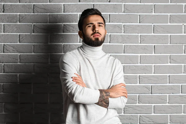 Young bearded man with crossed hands on grey brick wall background