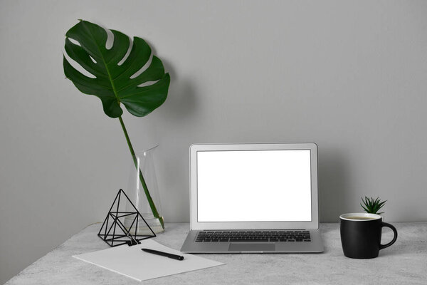 Workplace with laptop, cup and palm leaf in vase near light wall