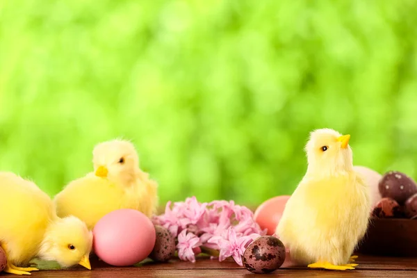 Cute chickens, Easter eggs and flowers on table outdoors