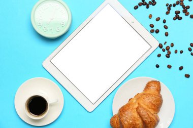 Bir fincan kahve, kruvasan, tablet bilgisayar ve mavi zemin üzerindeki çalar saatle kompozisyon
