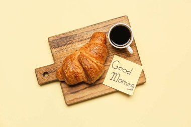 Bir fincan kahve, kruvasan ve yapışkan bir not. Renkli günaydın mesajı.