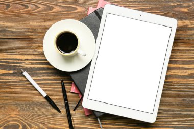Tablet bilgisayarlı kompozisyon, kırtasiye malzemeleri ve ahşap arka planda bir fincan kahve.
