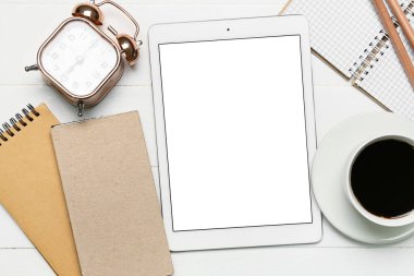 Tablet bilgisayarı, çalar saat, bir fincan kahve ve ahşap zemin üzerine kırtasiye malzemeleri.