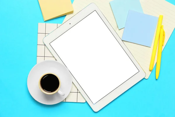 Composition with tablet computer, cup of coffee and stationery supplies on blue background