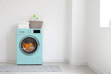 Çamaşır odasındaki beyaz duvarın yanında modern turkuaz çamaşır makinesi.