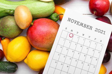 Farklı meyve, sebze ve takvimde beyaz ahşap arka planda Dünya Vejetaryen Günü işaretli.