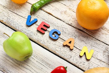 Farklı meyveler, sebzeler ve beyaz ahşap arka planda VEGAN kelimesi. Dünya Vegan Günü kavramı
