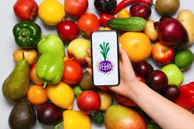 Taze meyveler, sebzeler ve elinde cep telefonu olan Gri arka planda 1 Kasım Dünya Günü yazılı bir kadın.