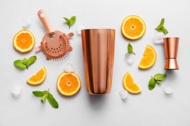 Bakır süzgeç, ayakkabı sallayıcısı, çifte jigger ve gri arka planda kokteyl malzemeleri.