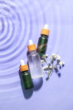 Bir şişe doğal serum ve leylak arkaplanda suyla çingene çiçeği.