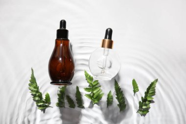 Beyaz zemin üzerinde su içinde doğal serum ve eğreltiotu yaprakları şişeleri