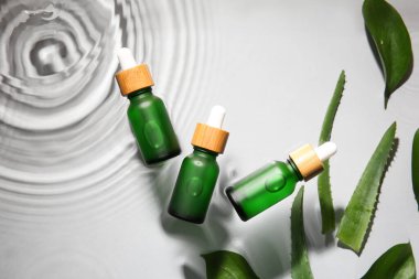 Beyaz zemin üzerinde su içinde doğal serum ve bitki yaprakları şişeleri