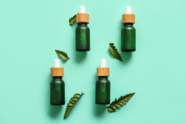 Renkli arkaplanda doğal serum ve eğrelti otu yaprakları şişeleri