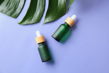 Leylak arka planında doğal serum ve palmiye yaprağı şişeleri.