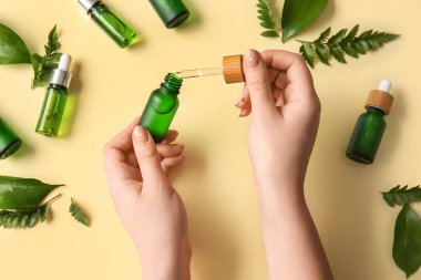 Doğal serum şişeleri ve bitki yaprakları olan kadın eller, yakın plan.