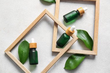 Doğal serum şişeleri, boş çerçeve ve açık arkaplanda bitki yaprakları olan kompozisyon