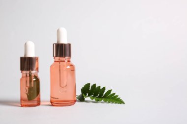 Beyaz zemin üzerinde doğal serum ve eğreltiotu yaprağı şişeleri