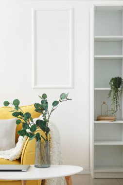 Oturma odasındaki masada okaliptüs dalları ve dizüstü bilgisayarlı vazo.