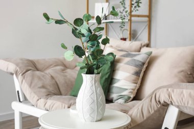 Oturma odasındaki kanepenin yanında okaliptüs dalları olan vazo.