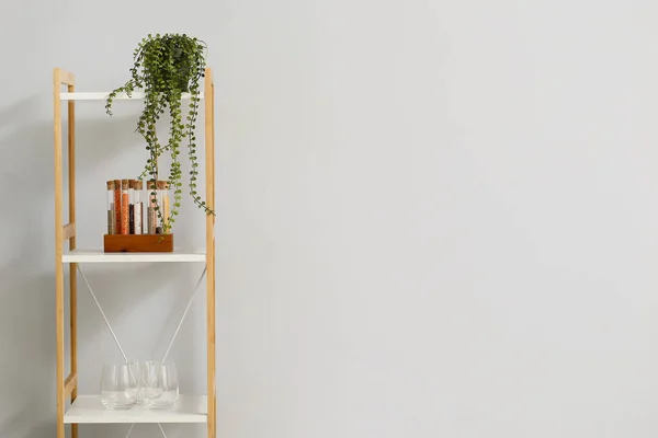 Shelf unit with empty glasses, spices and houseplant near light wall