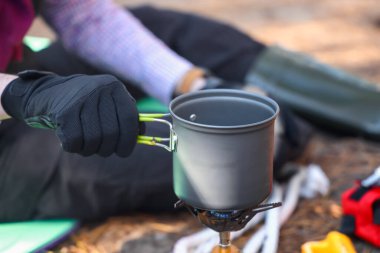Ormanda taşınabilir gaz ocağında yemek pişiren erkek turist, yakın plan.