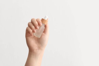 Beyaz arka planda serum şişesi olan kadın eli, yakın plan.
