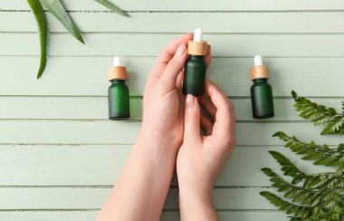 Renkli ahşap arka planda doğal serum şişeleri olan kadın eller, yakın plan.