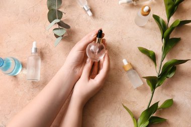 Farklı şişelerde doğal serum ve bitki dalına sahip kadın elleri.