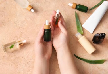 Renkli arka planda doğal serum şişeleri ve kozmetik ürünleri olan kadın elleri