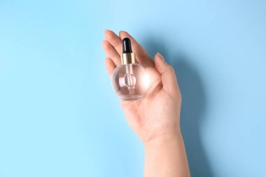 Mavi arka planda serum şişesi olan kadın eli, yakın plan.