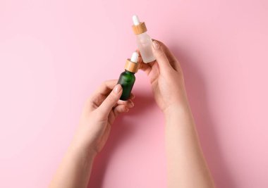 Pembe arka planda serum şişeleri olan kadın eller.