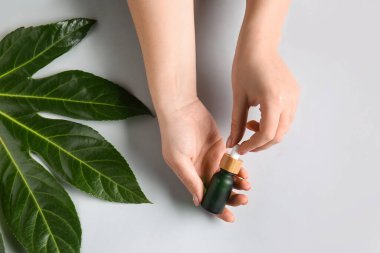Beyaz arka planda doğal serum ve bitki yaprağı olan kadın elleri, yakın plan.