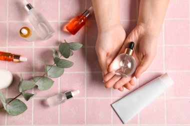 Farklı şişelerde doğal serum ve okaliptüs dallı kadın elleri.