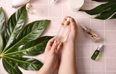 Doğal serum, kozmetik ve bitki yapraklarıyla dolu kadın elleri renkli fayanslarda.