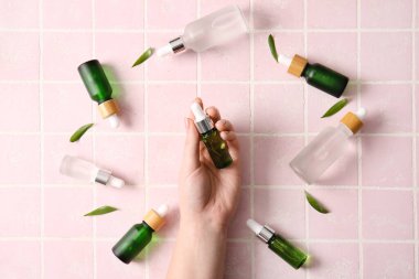 Fayansların üzerinde farklı doğal serumdan yapılmış farklı şişelerle kadın eli.