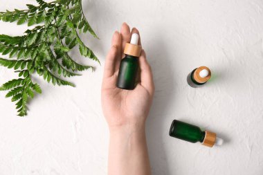 Doğal serumdan şişeler ve hafif arka planda eğrelti otu yaprağı olan bir kadın eli.