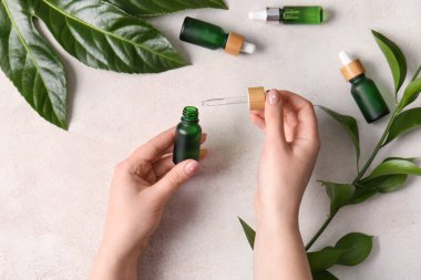 Doğal serumdan şişeler ve hafif arka planda bitki dalları olan kadın eller.