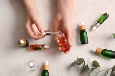 Işıklı arka planda farklı şişe doğal serumu olan kadın elleri.